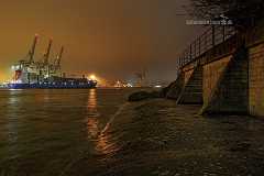 mauer Eine Kaimauer am Elbufer im Hafen Hamburg. Die Lichter des Hafens tauchen die feucht dunstige Nacht in eine gelbliche Szenerie. Im Hintergrund sieht man ein...