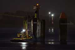 nachtschicht In dunkelster Nacht mach ein Boot mit drei Arbeitern am einem Dalben im Hafen fest. Zwei Leuchtfeuer im Hintergrund und das Positionslicht des Bootes stellen...