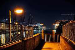 nightwalk Ausblick bei Nacht auf einer Fußgängerbrücke im Hamburger Hafen. Im Hintergrund Containerbrücken. Die von einer Laterne beleuchtete Brücke mit ihren hohen...