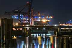 reflektionen Nächtliche Szenerie im Hafen. Ein Containerschiff liegt unter Containerbrücken deren Lichter sich im Wasser spiegeln. Eine Autobahnbrücke mit Leuchtspuren teilt...