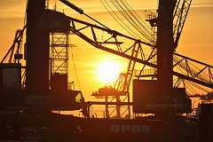 sundown_cranes Kurz vor Sonnenuntergang im Hafengebiet. Die gleißende Sonne steht rund und tief am Himmel und läßt die Krananlagen des Industriehafens im Gegenlicht als...