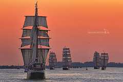 atlantis Fünf Großsegler segeln auf der Elbe vor orangerotem Himmel dem Sonnenuntergang entgegen.