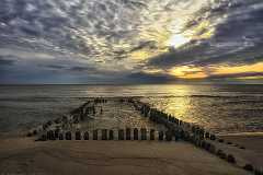 buhnen Buhnen am Strand von Rantum auf Sylt. Ein dekorativer Wolkenhimmel zieht vor der tiefstehenden Sonne vorbei deren Strahlen sich in der ruhigen Nordsee spiegeln.