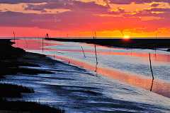 friedrichskoog Ein Sommerabend an der Nordseeküste. Die Sonne versinkt im Meer mit einem grandiosen Farbspiel am Himmel hinter der Hafeneinfahrt von Friedrichskoog.