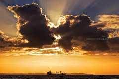 sunclouds Eine einzelne große Wolke verdeckt die tiefstehende Sonne über dem Meer. Sonnenstrahlen steigen hinter den Wolken empor zum Himmel. Ein Frachtschiff ist als...