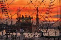 burning-sky Durch die Takelage der Dreimastbark Rickmer Rickmers im Hafen Hamburg führt der abendliche Blick nach Sonnenuntergang bei orangerotem Himmel durch Masten und...