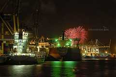 hafenfeuerwerk Im Industriehafen von Hamburg liegen mehrere bunt erleuchtete Containerschiffe am Kai unter Containerbrücken. Ein Feuerwerk im Hintergrund erleuchtet den...